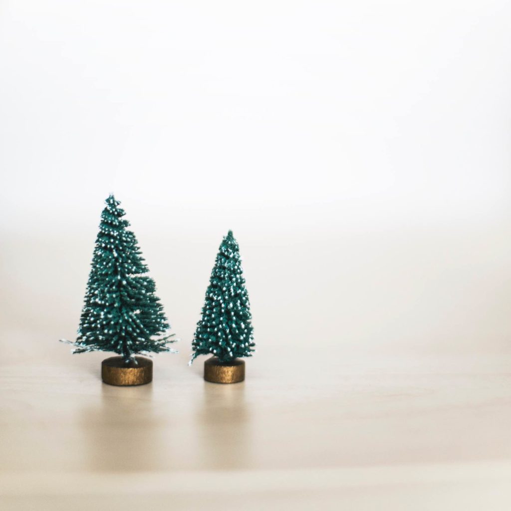 Zwei kleine Tannenbäume aus Plastik stehen vor einem beigen Hintergrund